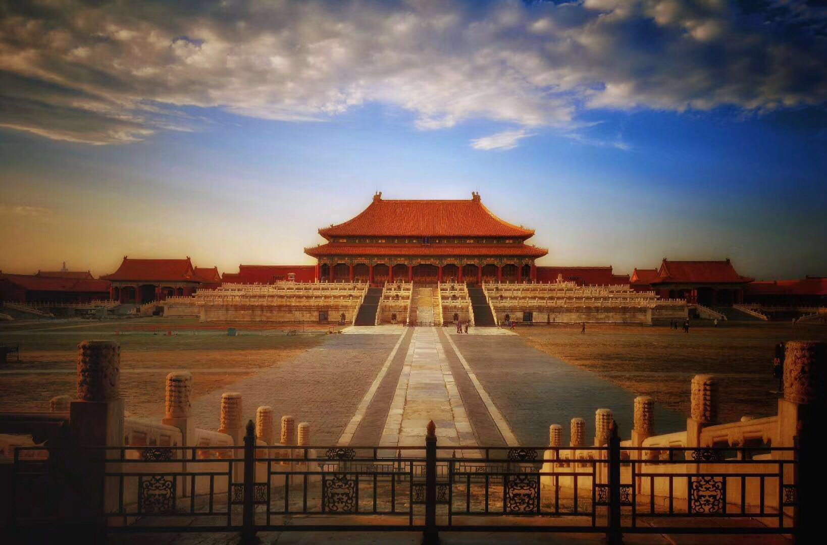 The Forbidden City’s grand palace courtyard beneath dramatic clouds in warm light