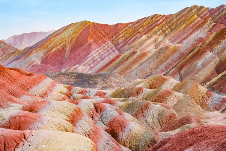 Layered red, gold, and cream-colored mountains beneath a pale blue sky